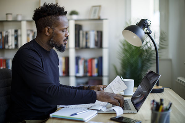 Adult male sitting at a desk while reviewing expenses and inputting into his laptop.